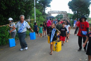水が入ったバケツをてんびん棒で担ぎ水の大切さをアピールする参加者ら＝6日、狩俣集落