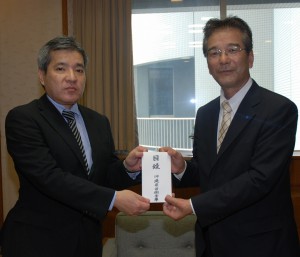 西理事長（右）から又吉知事公室長に支援金目録が手渡された＝13日、県庁知事公室