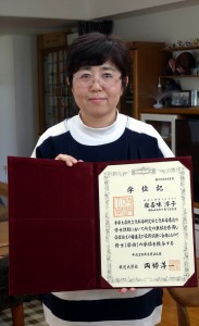 修士号を証明する「学位記」を手に笑顔を見せる座喜味淳子さん。充実の２年を振り返った＝１３日、平良西里の自宅で