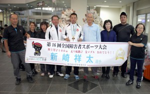 ２冠を達成した新崎選手（中央）を出迎える池間会長（右から４人目）や職場の同僚たち＝２５日、宮古空港