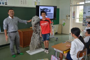 富山さん（左）は「人頭税石」の実物大の写真を使って昔の税について語った＝１５日、平一小学校
