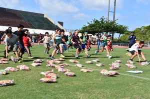 「お菓子ひろい」で一目散に走る笑顔の子どもたち＝11日、西原町民陸上競技場