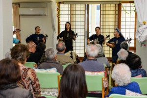 （左から）山本さん、瀬名波さん、川満さんと古謝さんの歌や三線を楽しんだ参加者ら＝31日、デイサービスひまわり