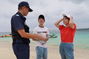 観光客らにリーフレットを配布し注意を促した＝27日、与那覇前浜ビーチ