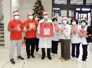 病院や同塾の関係者らが見守る中、與那覇代表（左から２人目）から本永院長（同３人目）に菓子が手渡された＝24日、宮古病院