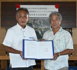 協定書を手にする三國常務（左）と花城会長＝16日、仲原公民館