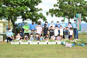 田場署長（後列右から３人目）から上地会長（同６人目）へ花が贈られた＝25日、池間添の児童公園