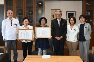 座喜味市長（右から３人目）から表彰状の伝達を受けた佐和田さん（左から３人目）と外間会長（同２人目）ら＝16日、市役所