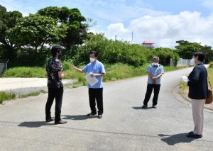 市の職員（左）から説明を受ける伊波氏（左から2人目）と市議たち＝６日、来間島の来間島マイクログリッド実証設備前