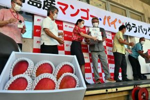 関係者が一列になって宮古島産のマンゴーとパインを手渡し、車両に積み込んだ＝14日、宮古郵便局