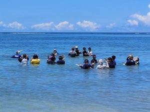 梶原さんらの指導を受けながら海に入る生徒たち＝11日、新城海岸