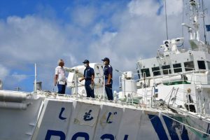 巡視船で福本部長（中央）から説明を受ける座喜味市長（左）＝15日、長山港