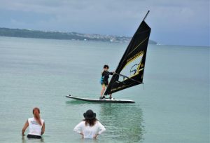 指導を受けてウインドサーフィンのボードに乗る児童＝23日、パイナガマビーチ