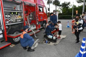 消防ポンプ車に搭載されている機材について職員の説明を聞きながら手に持ってみる子どもたち＝13日、市消防本部