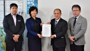 濱川会長（右から２人目）が大城教育長（同３人目）に協力依頼文を手渡した＝31日、市役所