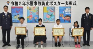 作品の前で記念撮影する入賞者の皆さん。左２人目から長田さん、久井さん、岸本さん、内間さん。左端は仲宗根署長＝24日、宮古島署