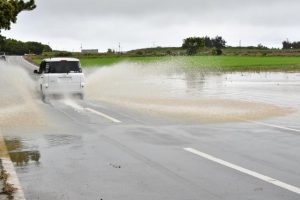 畑と道路が冠水し水しぶきを上げて走行する車＝30日、城辺吉野・一周道路（写真は一部加工してあります）