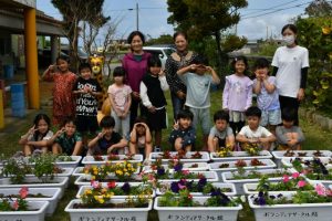 福島代表（後列右から５人目）らから花のプランターが贈呈された＝16日、伊良部こども園