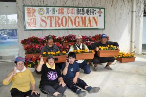 ストロングマンを歓迎する看板と丹精込めて育てた色鮮やかな花を設置し、笑顔を見せるみやこ学園の利用者ら=6日、宮古空港