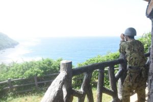 高台から双眼鏡で沿岸部を捜索する自衛隊員＝22日、伊良部前里添のさばおき園地