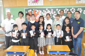 國仲会長（右）から入学祝い金と小学校生活への激励を受けて笑顔を見せる児童ら＝11日、狩俣小学校