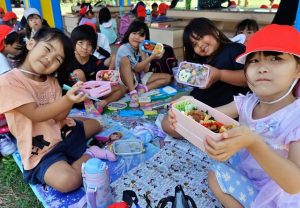 「見て見て、おいしそうでしょ」と母親手作りの弁当を自慢する児童たち＝２日、パイナガマ海空すこやか公園