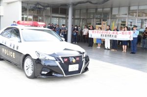 座喜味市長ら関係者が見送り、パトカーが先導し街頭パレードに出発した=6日、市役所