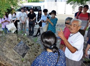 与那覇さんから当時の様子について説明を受けた祈念碑建立15周年の集い＝10日、上野野原