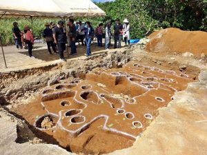 地元住民や多くの市民が訪れて発掘された遺構の説明に聞き入っていた＝7日、島尻元島遺跡内