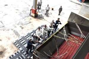 渡久山社長や関係者がサトウキビをベルトコンベヤーに投げ入れ操業が始まった=5日、多良間塩川の多良間工場