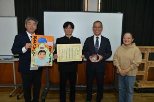 （写真左から）友利校長らが見守る中、赤嶺さんに下地本部長から表彰状が贈られた＝29日、西辺中学校