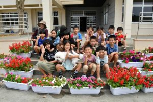 歓迎の思いを込めた花を前に笑顔を見せる子どもたち＝26日、宝塚医療大学宮古島キャンパス