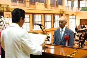 記念式典で砂川会長（左）から初代会長の喜屋武さんに功労賞が贈られた＝30日、砂川小学校