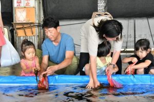新鮮なモズクを購入後つかみ取りを楽しむ親子ら＝２１日、宮古島漁業協同組合