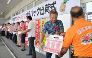関係者が一列になって宮古島産のマンゴーとパインを手渡し車両に積み込んだ「出荷式」=19日、宮古郵便局