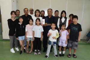 寄付金を手渡した狩俣ブンミャー会模合メンバーと受け取った狩俣子ども会の皆さん＝７日、狩俣集落センター