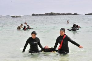 溺水者を救助し陸上に搬送して心肺蘇生法を施すまで一連の動きを訓練する参加者たち＝11日、シギラビーチ