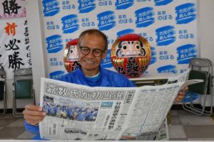 初当選から一夜明けて選挙結果を報じる宮古毎日新聞を手にし笑顔を見せる嘉数氏 =20日、平良西里の選挙事務所