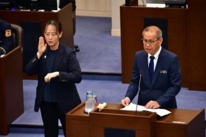 2025年度の施政方針を発表する嘉数市長。左は手話通訳者=27日、市議会議場
