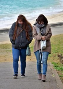 冷たい風に身をすくませて歩く女性ら＝８日、パイナガマビーチ