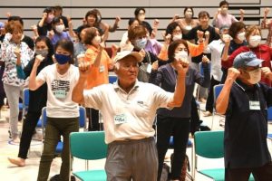 「ワイドー」の曲に合わせ体を動かす参加者ら＝20日、市未来創造センター多目的ホール