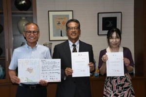 （左から）嘉数市長から教育長辞令を受ける宮城氏、教育委員の東風平氏＝７日、市役所