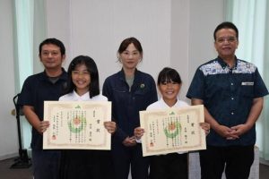 久志本部長（右）から表彰を受けた最優秀賞の喜納さん（同2人目）、優秀賞の仲里さん（同4人目）ら＝26日、JA宮古地区本部