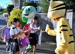かえるくん、トラくんとあいさつやハイタッチをする児童たち＝27日、鏡原小校門前