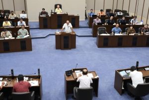 今年度の出張回数や市民報告などについて答弁する嘉数市長=25日、市議会議場