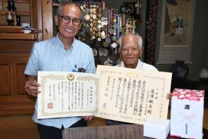 亀濱さん（右）に内閣総理大臣から贈られた祝い状などを手渡す嘉数市長＝８日、平良西里の亀濱さんの自宅