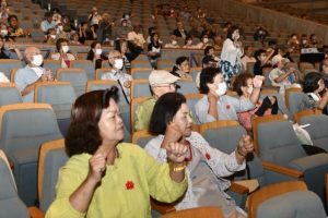 「ちゃーがんじゅう体操」を一緒に踊る高齢者ら＝12日、マティダ市民劇場