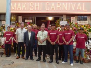 安里社長（前列右）ら関係者が集い、行われた「ＭＡＫＩＳＨＩ　ＣＡＲＮＩＶＡＬ」開業セレモニー＝16日、那覇市
