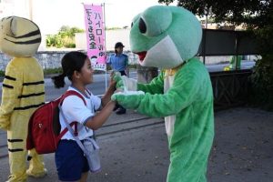 かえるくん、トラくんとあいさつを交わす児童たち＝14日、鏡原小校門前