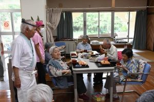 平良代表（左）が握ったすしに舌鼓を打ち笑顔を見せる利用者たち＝１日、小規模多機能型居宅介護事業所たかやま